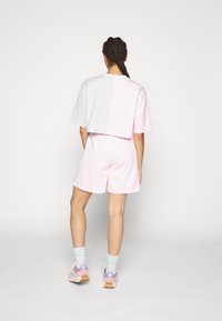 En kortärmad t-shirt i vitt och rosa med färgblockering, matchad med rosa shorts. Bärs med pastellrandiga strumpor och ljusrosa löparskor.