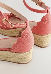 Sandales compensées corail rose avec brides à la cheville, bords festonnés, broderie florale et semelles plateformes en jute tressée.