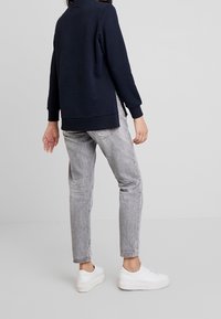 Felpa navy con maniche lunghe e polsini a costine, abbinata a jeans in denim grigio chiaro. Sneakers bianche completano il look.