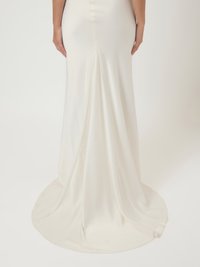 Μακρύ, εφαρμοστό φόρεμα από μαλακό, λευκό ύφασμα με ελαφριά γυαλάδα. Διαθέτει ουρά και διακριτικές ραφές στο πίσω μέρος. Λείος υφής.