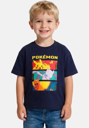 Jeune garçon souriant portant un t-shirt Pokémon bleu marine présentant Pikachu, Mewtwo et Dracaufeu avec un texte jaune au-dessus.