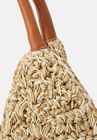 Close-up van een geweven beige en lichtbruine strooien tas met gladde tan leren handvatten.