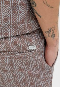 Smeđi tkanina s uzorkom i plavim geometrijskim oblicima, s stražnjim džepom i etiketom koja glasi "JACK & JONES EST.1990."