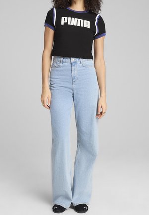 Czarna krótka koszulka z białym logo "PUMA" i fioletowymi akcentami, w połączeniu ze światłoniebieskimi spodniami z wysokim stanem i szerokimi nogawkami oraz czarnymi skarpetkami.