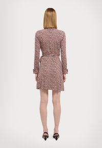 Robe à motifs rouges et blancs avec manches longues, taille nouée, et jupe évasée au-dessus du genou. Tissu lisse avec un léger éclat.