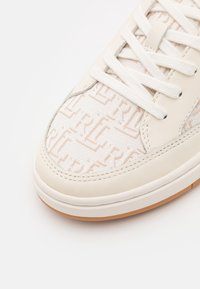 Vit sneaker med en texturerad överdel i tyg med ett geometriskt mönster, läderdetaljer och vita snören; gummisula.