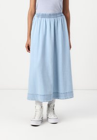 Gonna di jeans azzurra chiara con vita elasticizzata arricciata, che arriva a metà polpaccio; abbinata a sneakers bianche alte e calzini a costine.