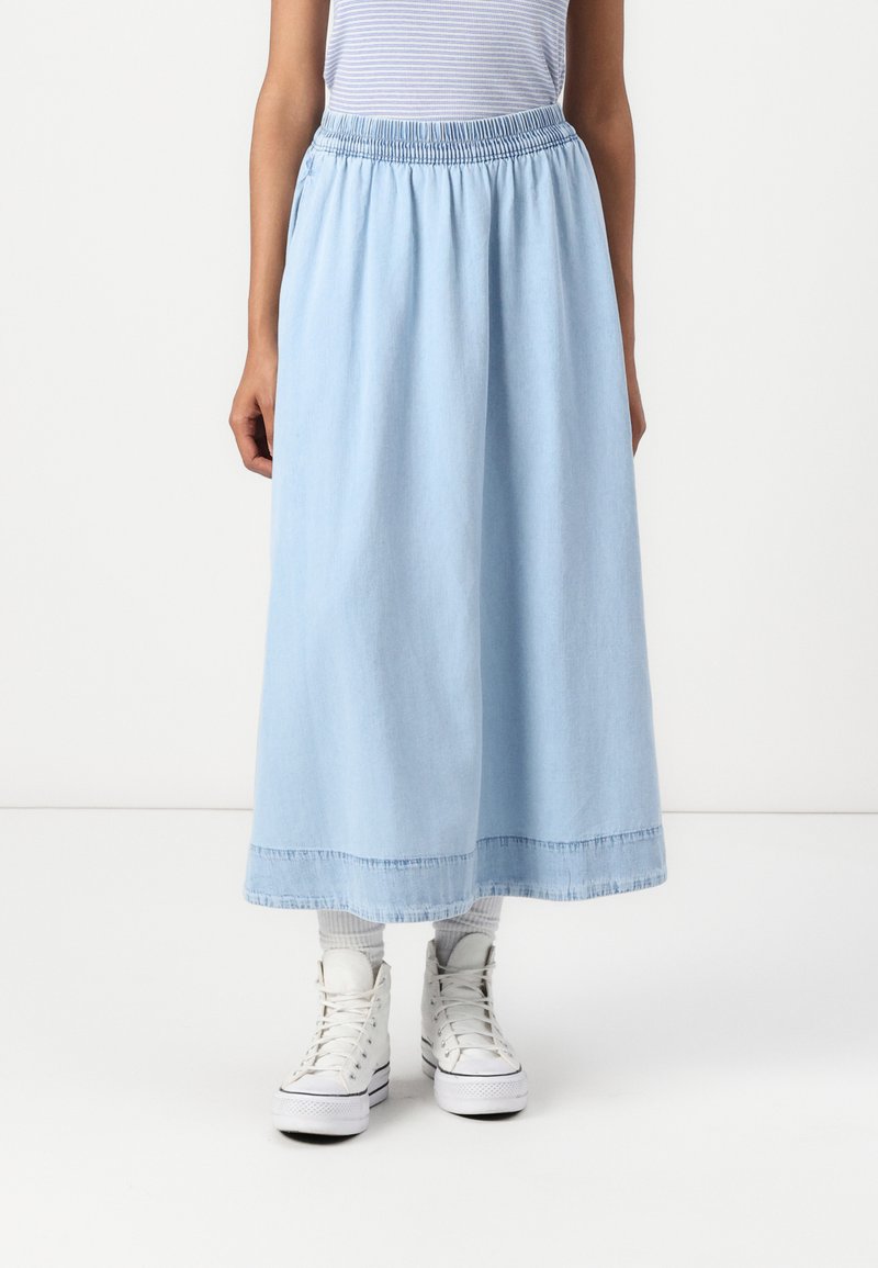 Gonna di jeans azzurra chiara con vita elasticizzata arricciata, che arriva a metà polpaccio; abbinata a sneakers bianche alte e calzini a costine.