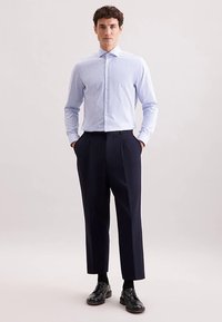Camicia a righe blu e bianche con colletto button-down, abbinata a pantaloni plissettati blu navy e scarpe eleganti nere. Vestibilità liscia e sartoriale.