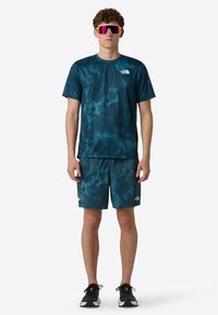 A teal tie-dye athletic shirt and matching shorts, made of lightweight fabric, paired with black sneakers and large reflective sunglasses.