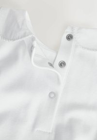 Witte katoenen kleding met een kraag, voorzien van drukknoopsluitingen. Soepele textuur en nette stikdetails.