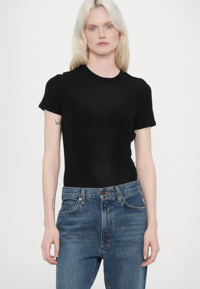 Maglietta nera a maniche corte realizzata in tessuto trasparente, design aderente con scollo rotondo. Abbinata a jeans in denim blu a vita alta.