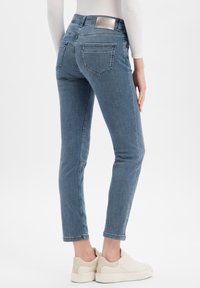 Jean denim bleu skinny vu de dos, avec une taille haute, deux poches arrière et une étiquette métallique de la marque à la ceinture.
