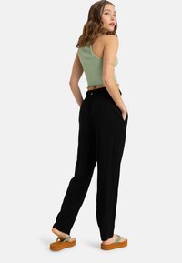 Pantaloni neri larghi con tasche laterali, abbinati a un crop top a coste verde menta. Il modello indossa sandali con plateau color sabbia.