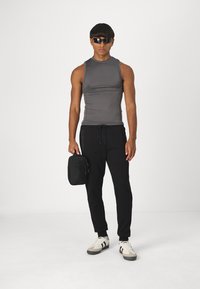 Grå ærmeløs skjorte, sorte tætsiddende sweatpants med snor, hvide sneakers med sorte striber og en sort lynlåst taske.