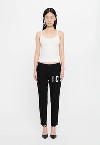 Witte aansluitende tanktop, gecombineerd met hooglopende zwarte jeans met gedurfde witte letters. Zwarte stilettoschoenen maken de look compleet.