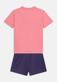 Πίσω όψη ενός κοντομάνικου ροζ μπλουζάκι συνδυασμένου με σκούρο μπλε σορτς, παρουσιασμένο σε απλό φωτεινό φόντο.