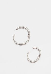 Un paio di piccoli orecchini a cerchio in argento con ganci aperti su uno sfondo bianco semplice.
