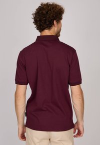Polo shirt marron à manches courtes, col texturé et fentes latérales discrètes. Tissu lisse, coupe classique et détails de coutures soignées.
