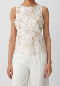 Blomstermönstrad spetsblus i beige och kräm, ärmlös design, rund halsringning, semi-genomskinlig textur, tillsammans med vita vida byxor.