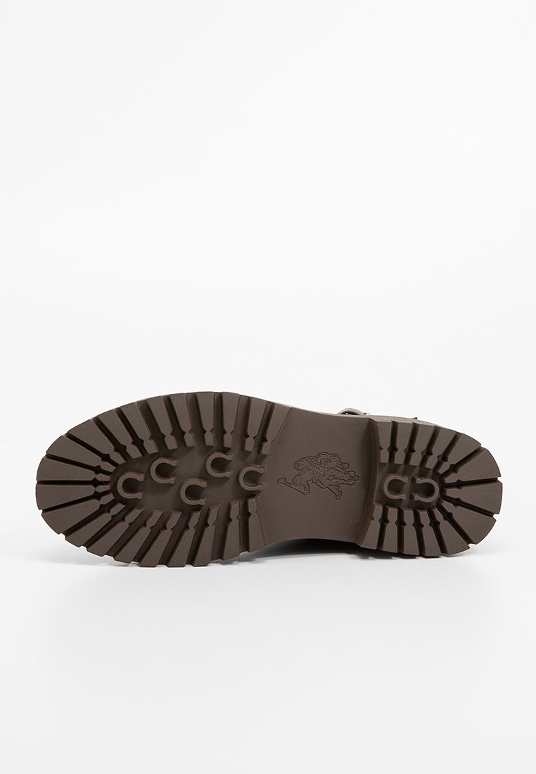Semelle en caoutchouc brun avec un motif de semelle profonde, comportant des accents circulaires. Surface texturée avec le logo au centre.