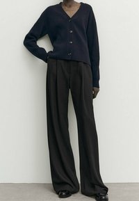 Cardigan côtelé bleu marine avec un col en V et des boutons noirs, associé à un pantalon noir large à taille haute. Tissu lisse et coupe décontractée.