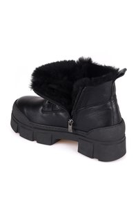Botas de tobillo de cuero negro con ribete de piel sintética, cierre de cremallera, suela gruesa, punta redonda y suela de goma texturizada. Acabado suave y diseño robusto.