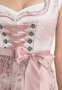 Robe en soie rose avec un corsage à lacets, des boutons décoratifs, un tissu texturé et un ruban noué à la taille orné de perles.