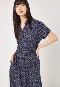 Kleid mit Marine-Muster, Kragen, kurzen Ärmeln, elastischem Taillengummi und Taschen. Mit einem floralen geometrischen Design in Weiß.