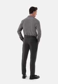Graues Langarmhemd mit Kragen, kombiniert mit dunkelgrauen Hosen mit strukturiertem Muster und einem knöpfbaren Gesäßtasche, getragen mit schwarzen Schuhen.