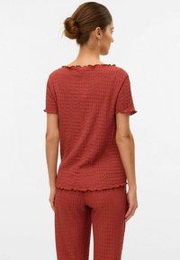 Haut rouge en coton texturé à manches courtes avec un décolleté festonné, porté avec un pantalon assorti. Le tissu présente un motif froissé et une coupe ample.