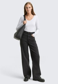 Zwarte wijde jeans gecombineerd met een aansluitend wit shirt met lange mouwen. Een zwarte slouchy handtas en fors zwart schoeisel maken de look compleet.