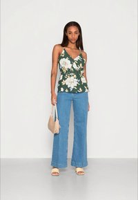 Top verde com padrão floral e design envolvente, combinado com jeans de perna larga azuis claros. Inclui uma bolsa bege e sandálias em tons claros.