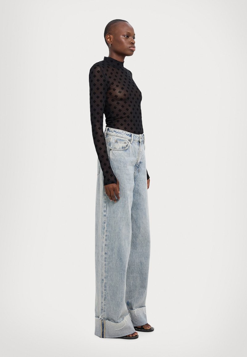 Top negro transparente de mangas largas con un patrón de puntos, combinado con jeans de pierna ancha en azul claro que presentan un dobladillo deshilachado y detalles en los puños.