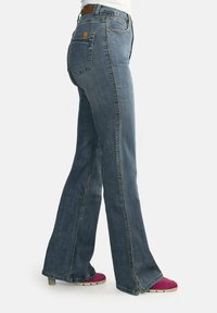 Jeans de mezclilla azules acampanados con cintura alta, sutil desgaste en los muslos y un parche de cuero marrón en la parte trasera de la cintura.