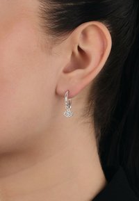 Orecchino a cerchio in argento con un piccolo design a occhio e una gemma trasparente centrale. Texture liscia, finitura lucida e forma contemporanea in mostra.