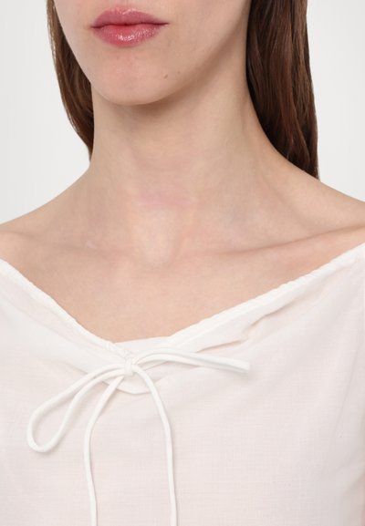 White, lightweight blouse with an off-the-shoulder neckline, featuring a drawstring tie detail at the front and a soft, smooth texture.