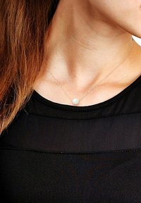 Collier en argent avec un pendentif en perle blanche unique, porté sur un haut noir. La chaîne est délicate et a une texture fine.