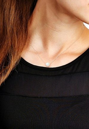 Collier en argent avec un pendentif en perle blanche unique, porté sur un haut noir. La chaîne est délicate et a une texture fine.