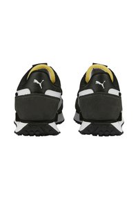 Black athletic shoes with suede and mesh material, white accents, and a textured outsole featuring circular grip patterns. Yellow inner lining.