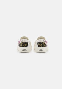 Une paire de baskets Vans blanches avec des motifs floraux et des patchs de talon noirs ornés de motifs floraux jaunes, vue de l'arrière sur un fond blanc.