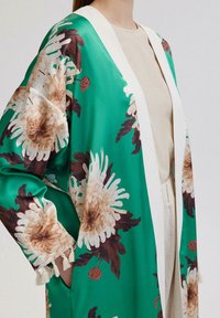 Roheline lilleline kimono, millel on suured valged ja pruunid krookuselõngad, valge äär, kerge kangas ning tupsudetailid varrukatel.