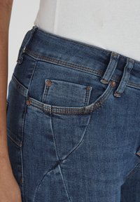 Jeans en denim bleu foncé avec une coupe ajustée, des coutures visibles, des poches avant et un motif de couture unique pour un détail supplémentaire.