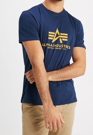 T-shirt en coton bleu marine avec un logo imprimé jaune comprenant des lettres stylisées et des rayures horizontales, col rond et manches courtes.