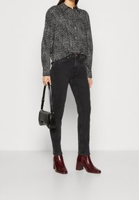 Mustavalkokuvioinen nappitettava paita, mustat korkevyötäröiset farkut, viininpunaiset korkokengät ja pieni musta käsilaukku.