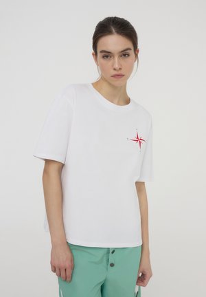 T-shirt bianco in cotone a maniche corte, con un design di una bussola rossa sul petto. Vestibilità ampia, scollatura rotonda, tessuto morbido.