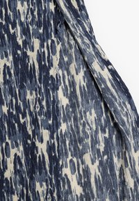 Tessuto con un motivo astratto blu e crema. Presenta una texture morbida e leggera, con una superficie stropicciata che si drappeggia elegantemente.