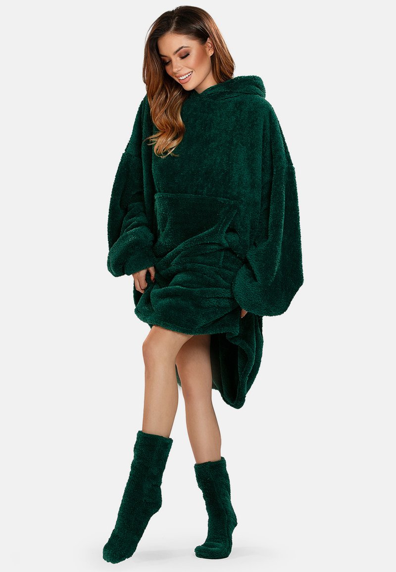 Poncho verde in pile con cappuccio, maniche oversize, tasca frontale e calzini coordinati. Texture morbida, lunghezza fino a metà coscia, senza motivi visibili.