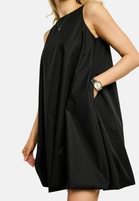Fekete, ujjatlan ruha laza, A-vonalú sziluettel, sima anyagból készült. Zsebekkel és a szegélyen megkötött részlettel rendelkezik.