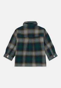 Chemise en flanelle à carreaux verts et gris, avec un col, des poignets boutonnés et un détail en yoke à l'arrière. Présente des accents jaunes dans le motif.